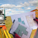 Land surveyor holds a bunch of documents while his equipment sits in front of him